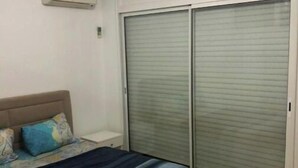 Une chambre à coucher comprenant un lit, une tête de lit, une table de chevet, une lampe, une fenêtre et un placard avec des portes coulissantes.