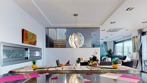 Un salon moderne avec une table basse en verre, un grand tableau abstrait et un luminaire au plafond original.
