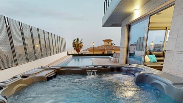 Une piscine sur le toit, dotée de jacuzzis, d’une balustrade en verre et offrant une vue sur un immeuble dont le toit est recouvert de tuiles.