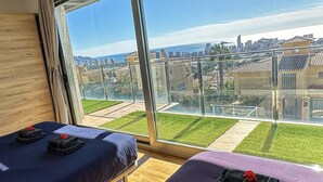 Une chambre avec deux lits, une grande fenêtre donnant sur un paysage urbain et une piscine.