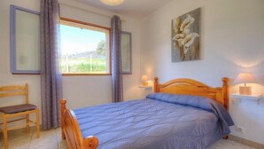 Ein Schlafzimmer mit einem hölzernen Bett, einem Sessel, einem Fenster mit Vorhängen, einem Gemälde und Nachttischlampen.