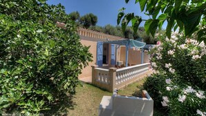 Eine Villa mit überdachter Terrasse, umgeben von üppiger Vegetation und blühenden Pflanzen.