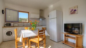 Eine kleine Küche mit Esstisch, Stühlen, einer Waschmaschine, einem Kühlschrank, einer Mikrowelle und einem Fernseher auf einem Holzständer.