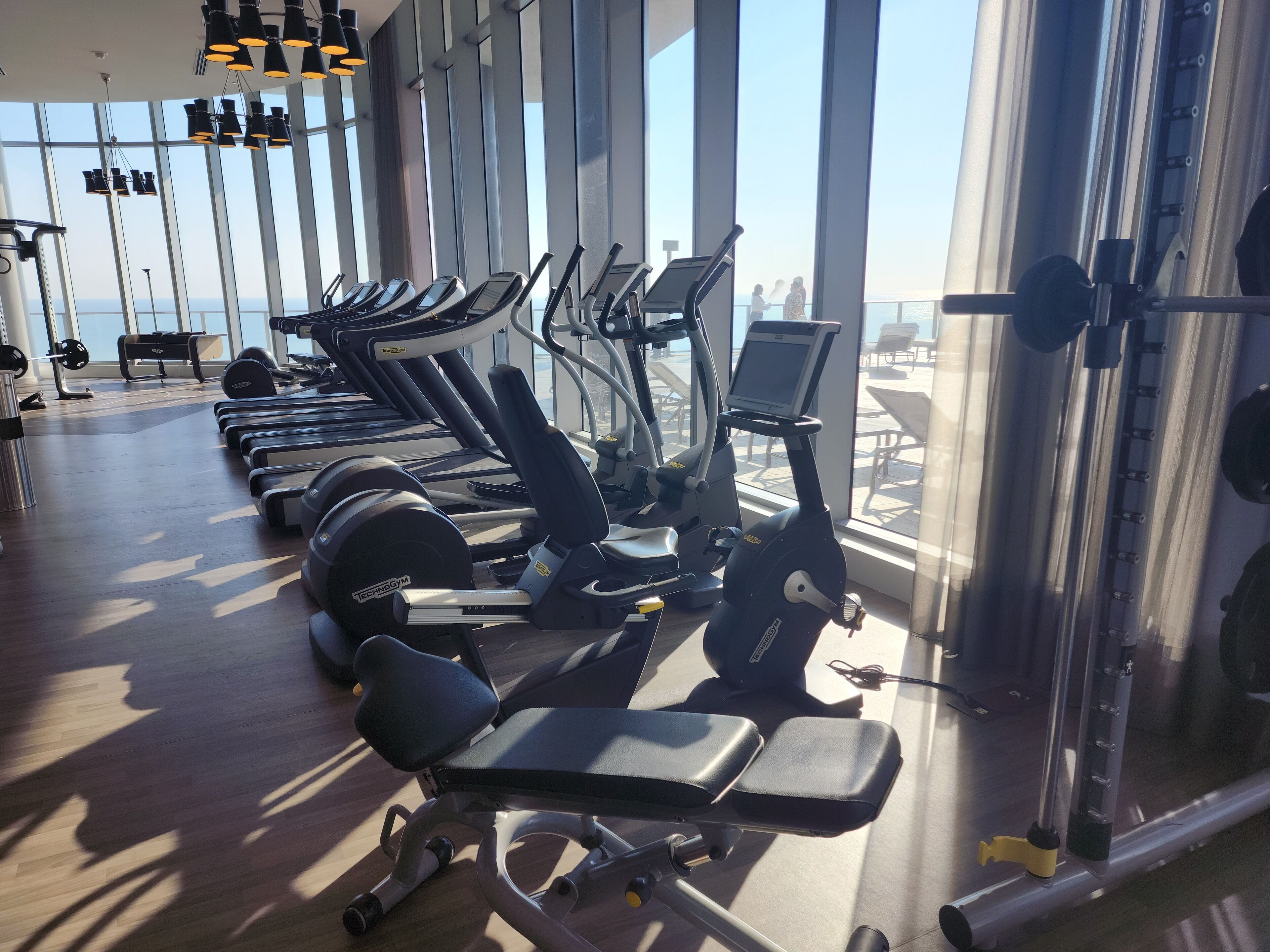 Ein Fitnessstudio mit Laufbändern, Kraftgeräten und Meerblick durch große Fenster.