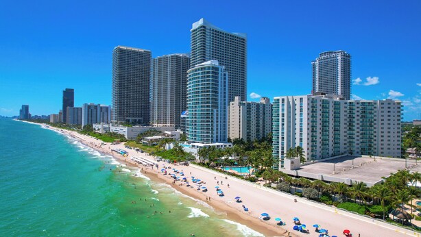 Un paisaje urbano costero con rascacielos, una playa de arena y un cielo azul despejado.
