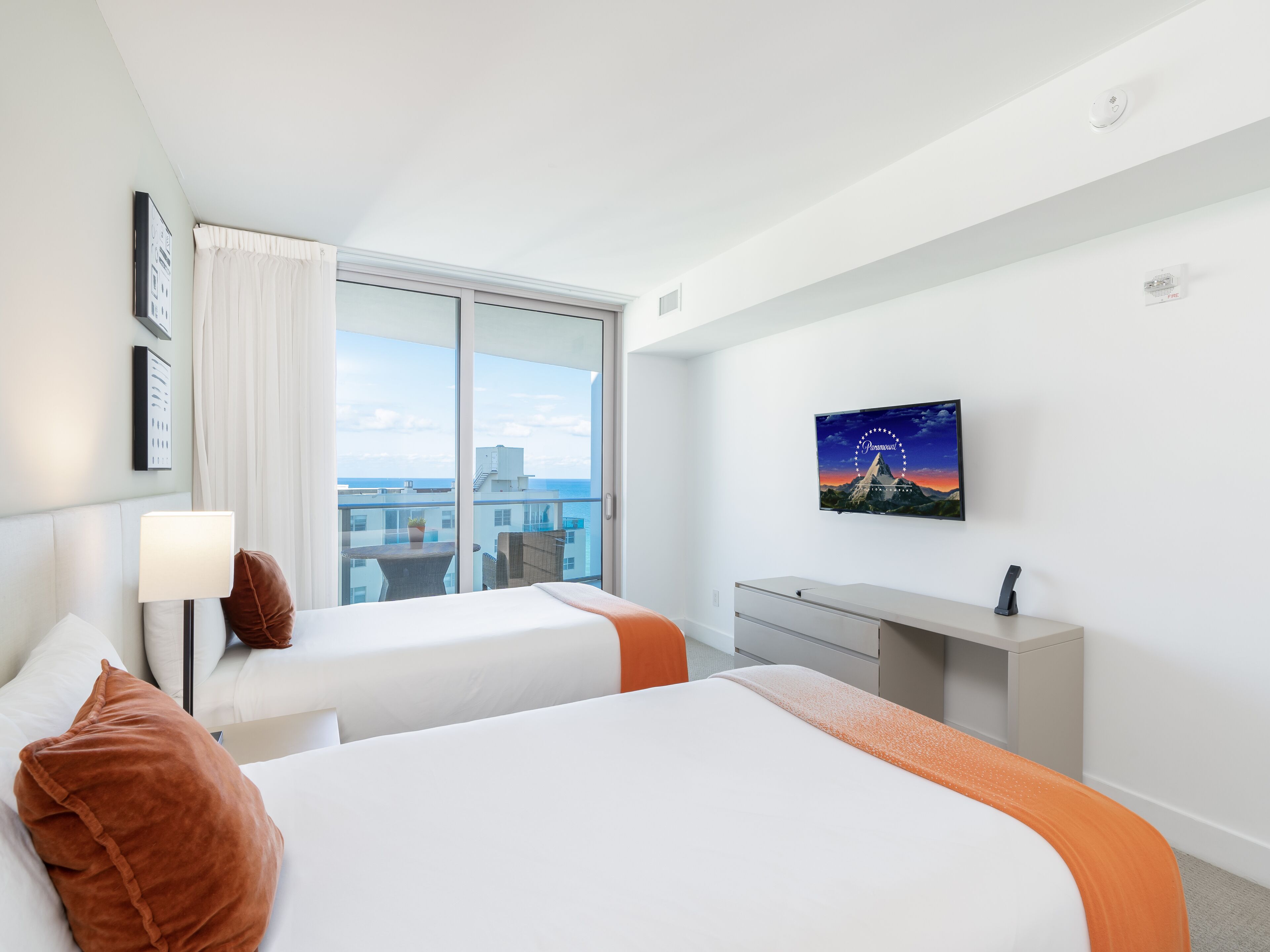 A hotel room with two beds, a desk, a TV, and a window with a city view.