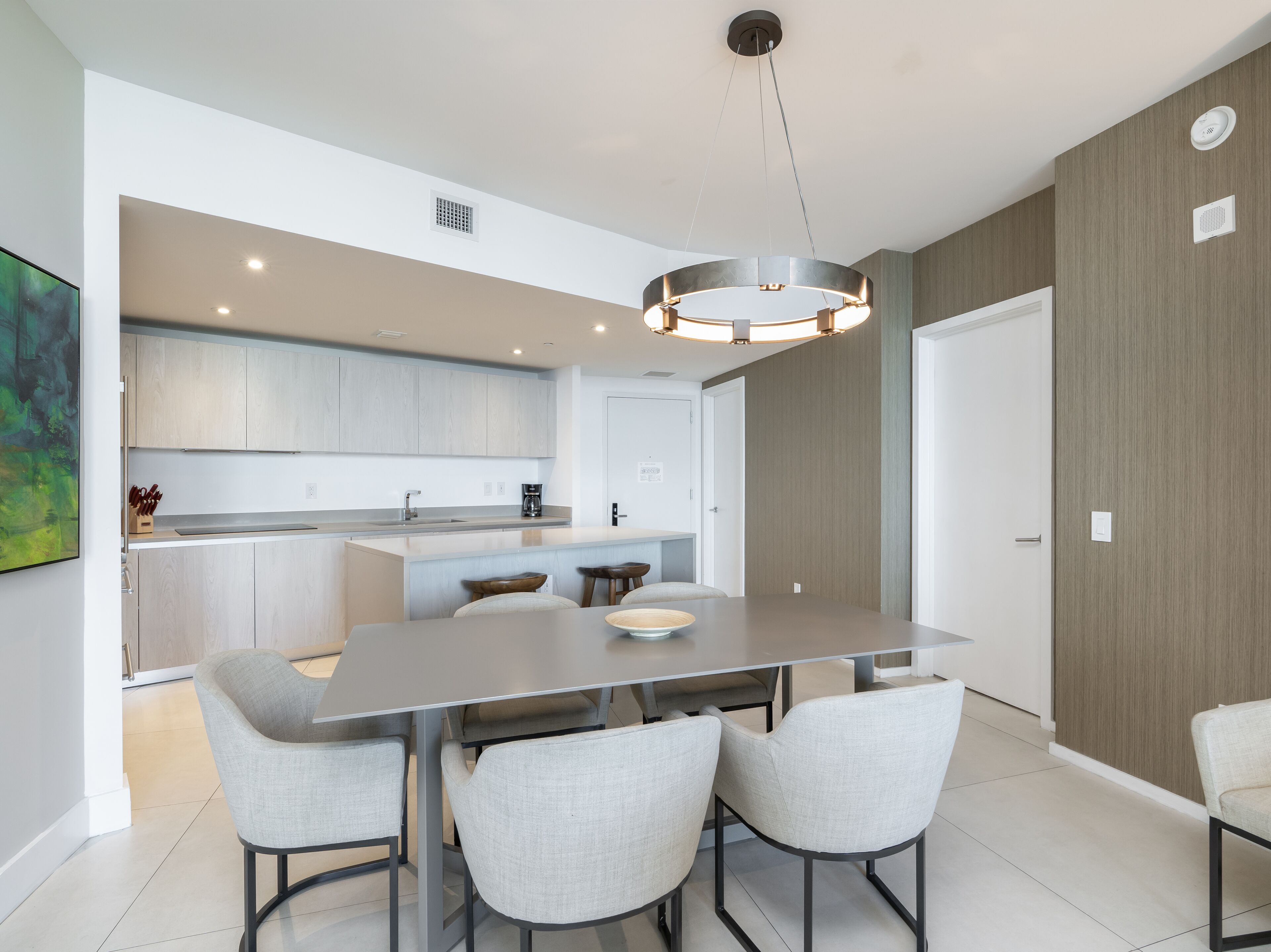 Una cocina moderna con gabinetes grises, una isla central y un comedor con una mesa y cuatro sillas.