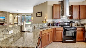 A modern kitchen with granite countertops, wooden cabinets, stainless steel appliances, and a large island with seating. - Heatable pool and Spa, propane grill, 3 King beds, 4 Twins, TV each bedroom (Kissimmee)