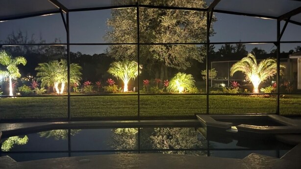 A pool area with a view of a garden illuminated by lights, a covered structure, and a reflection in the water. - Heatable pool and Spa, propane grill, 3 King beds, 4 Twins, TV each bedroom (Kissimmee)