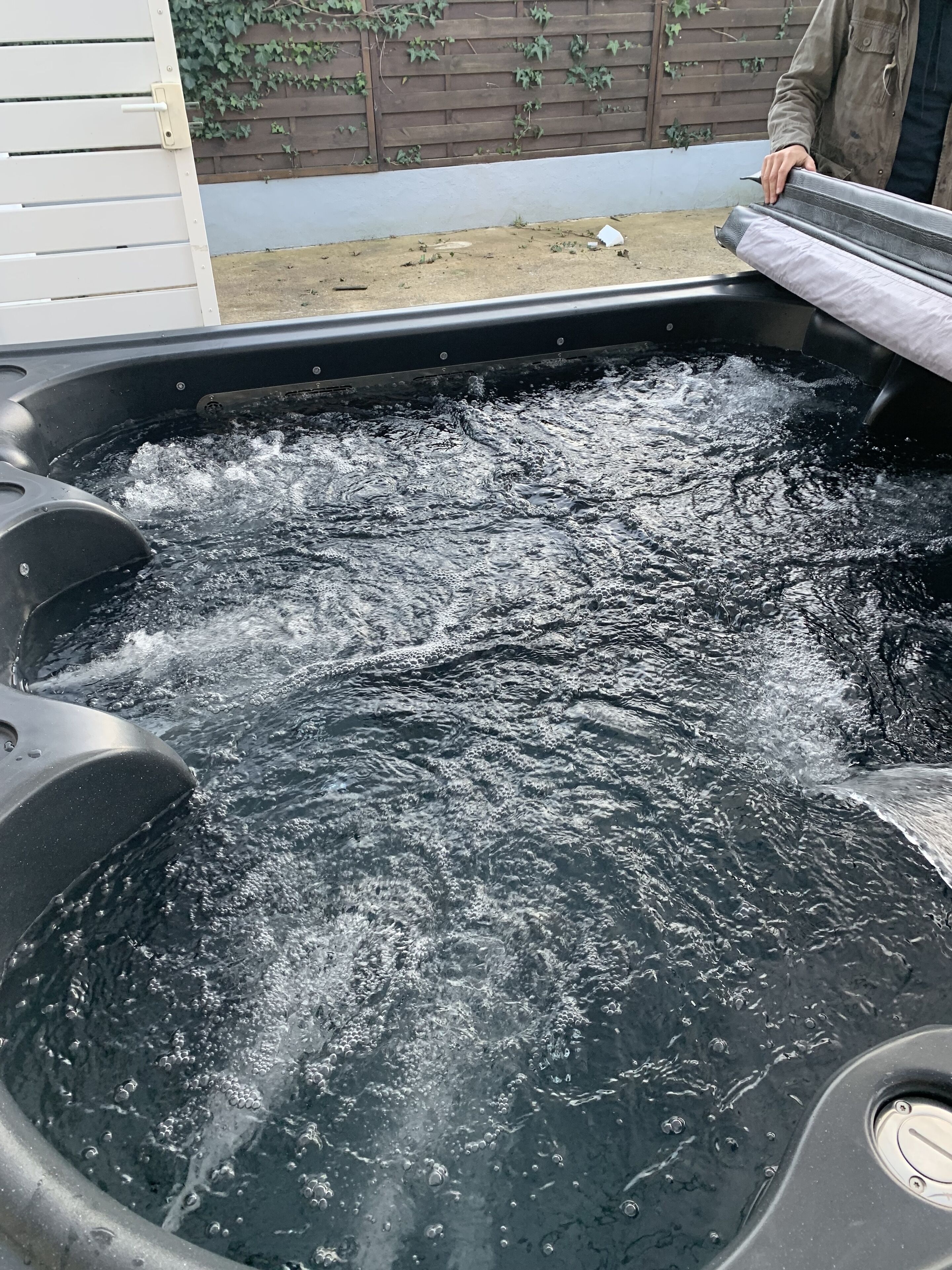A hot tub with water flowing, surrounded by a wooden fence and a white wall.