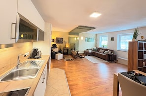 Una cocina moderna con estufa integrada, un comedor con mesa y sillas, una sala de estar con sofá y mesa de centro, y ventanas amplias que ofrecen luz natural.