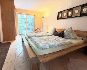 Un dormitorio con una cama de madera, vistas al exterior a través de un ventanal y una lámpara fijada a la pared.
