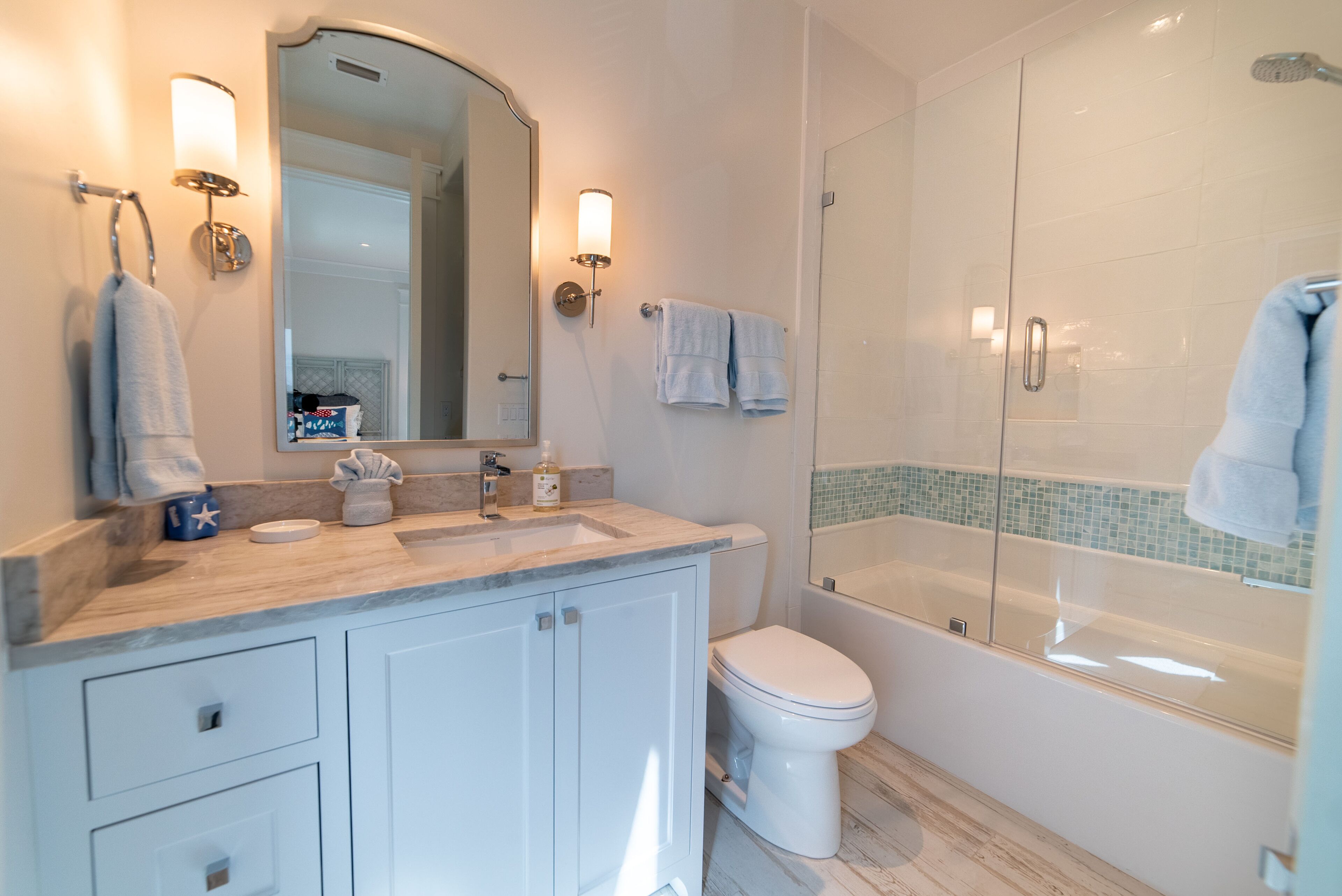 Une salle de bain moderne avec un comptoir en marbre, des toilettes blanches, une douche en verre et un grand miroir.