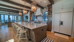 A spacious kitchen with a large island, wooden cabinets, and pendant lighting. - Luxury beach-front home, gourmet kitchen, private pool, gated community, gear (Port Saint Joe)