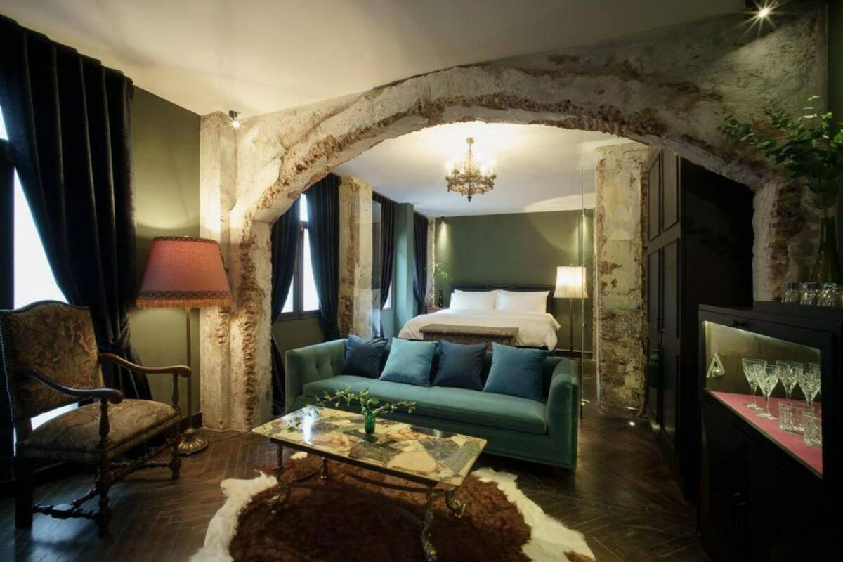 A room with a bed, a sofa, a chair, a table, and a chandelier.