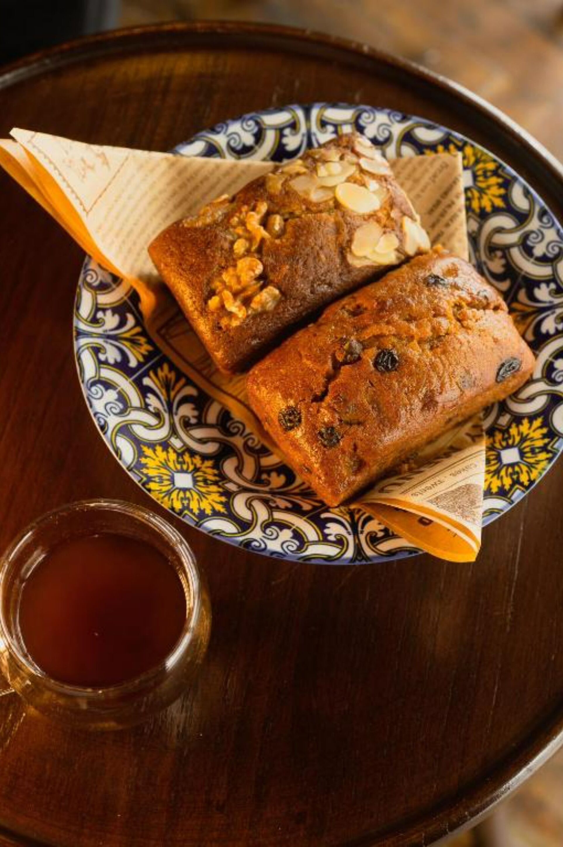 Two loaves of fruitcake on a decorative plate with a glass of tea.