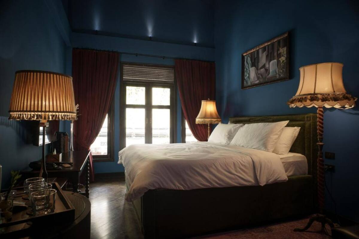 A bedroom with a bed, two lamps, a window with curtains, and a painting on the wall.