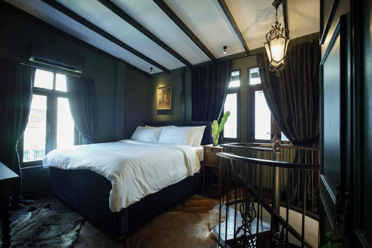 A bedroom with a large bed, a nightstand, a lamp, and a view of the outside through a window.