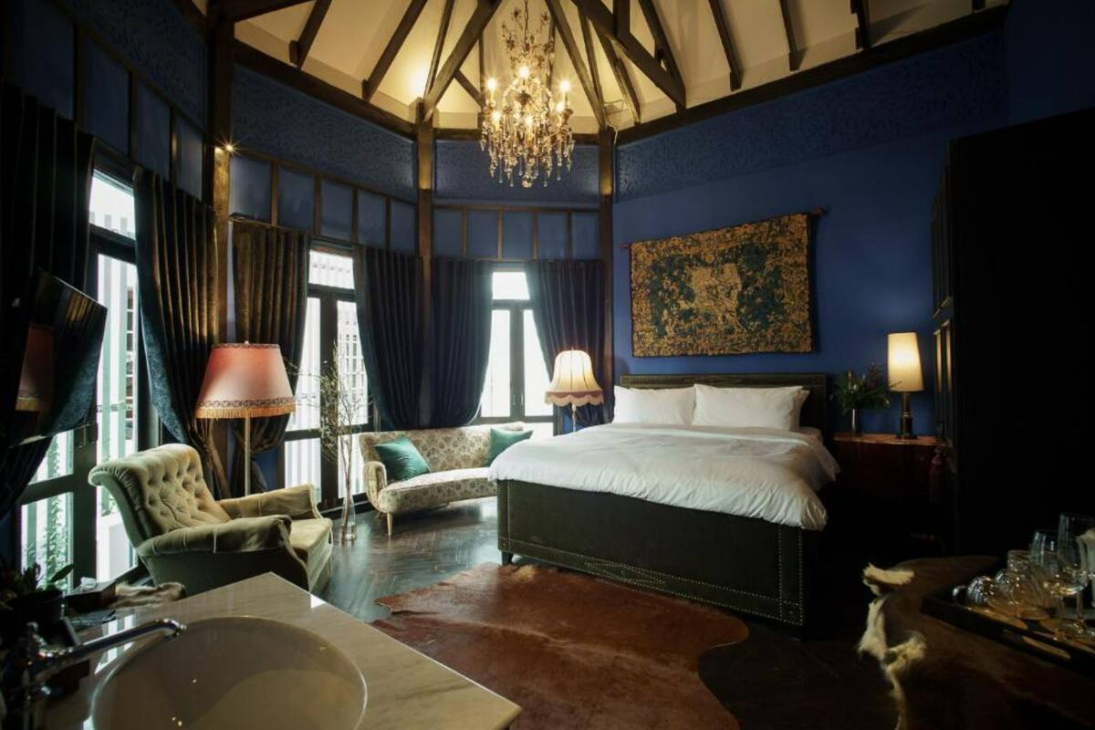 A room with a large bed, a chandelier, a sofa, and a dining table with glasses.