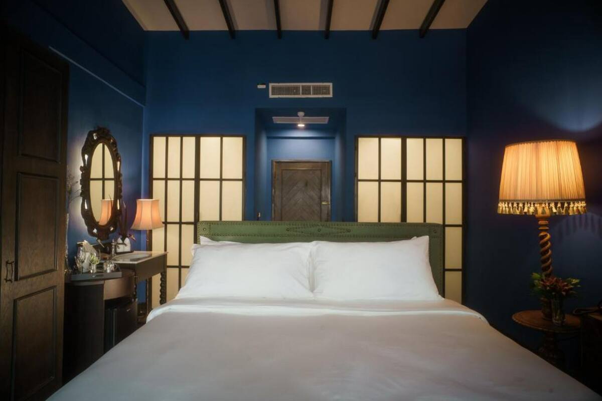 A hotel room with a bed, a nightstand with a lamp, a dresser, and a mirror.