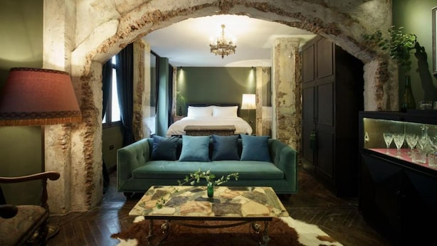 A room with a rustic stone archway, a green sofa, a wooden coffee table, and a bed with white linens. - Baan Tuk Din Hotel (Bangkok)