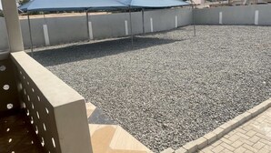 Un espacio al aire libre cubierto con suelo de grava, un muro de concreto y un edificio al fondo.