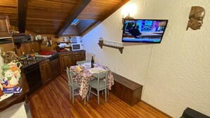 Une cuisine chaleureuse avec des meubles en bois, une table à manger avec des chaises et un téléviseur fixé au mur.