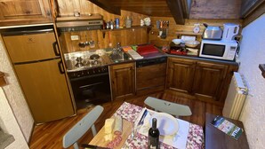 Une cuisine compacte avec des meubles en bois, un réfrigérateur, une cuisinière et un four à micro-ondes. On y trouve une table à manger dressée avec des assiettes, une bouteille de vin et un couteau.