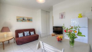 A living room with a sofa, TV, and a table with fruit and flowers. - L' Amandier with communal swimming pool (AJACCIO)