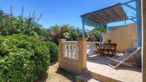 A covered outdoor seating area with a table and chairs, a pergola, and a garden with various plants and flowers. - L' Amandier with communal swimming pool (AJACCIO)