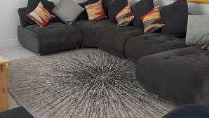 A modern living room with a sectional sofa, colorful throw pillows, a large mirror, and abstract wall art.