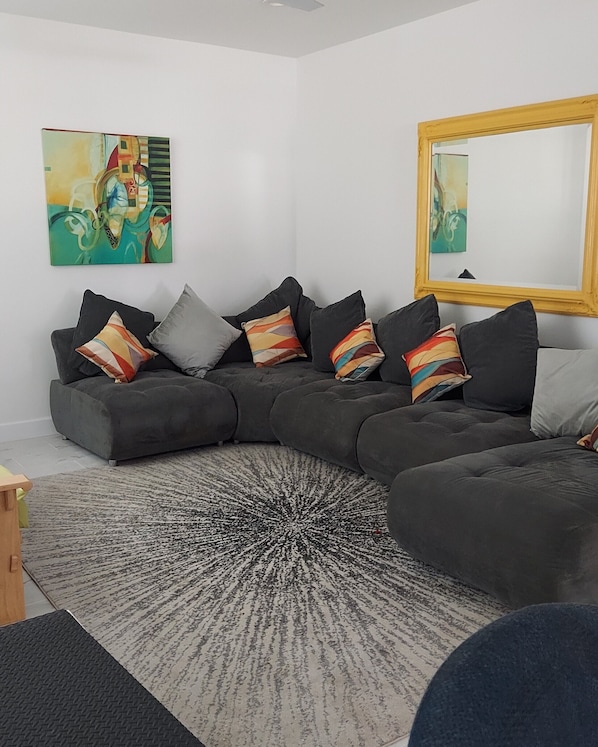 A modern living room with a sectional sofa, colorful throw pillows, a large mirror, and abstract wall art.