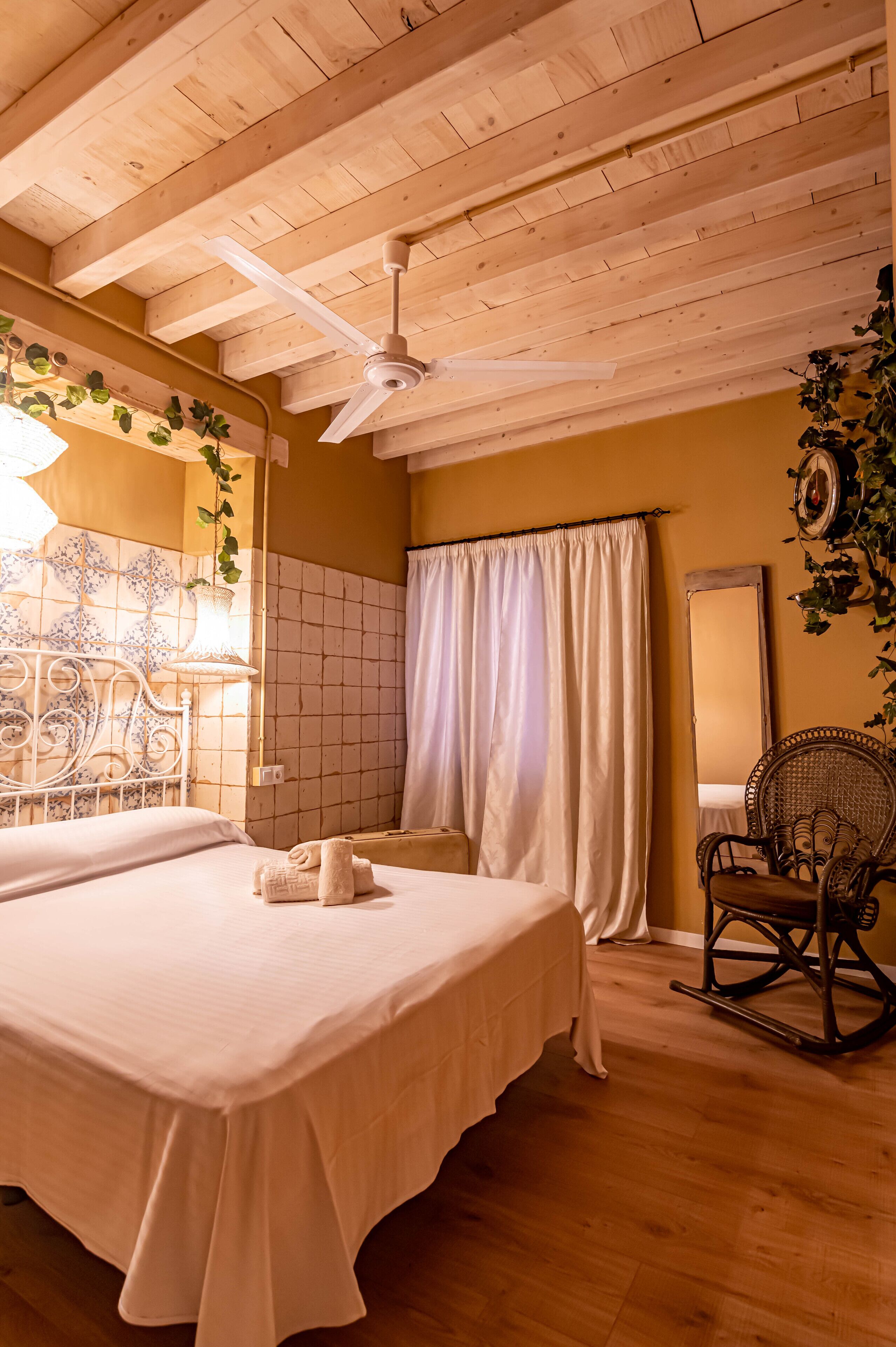 A room with a bed, a ceiling fan, a chair, and a mirror.