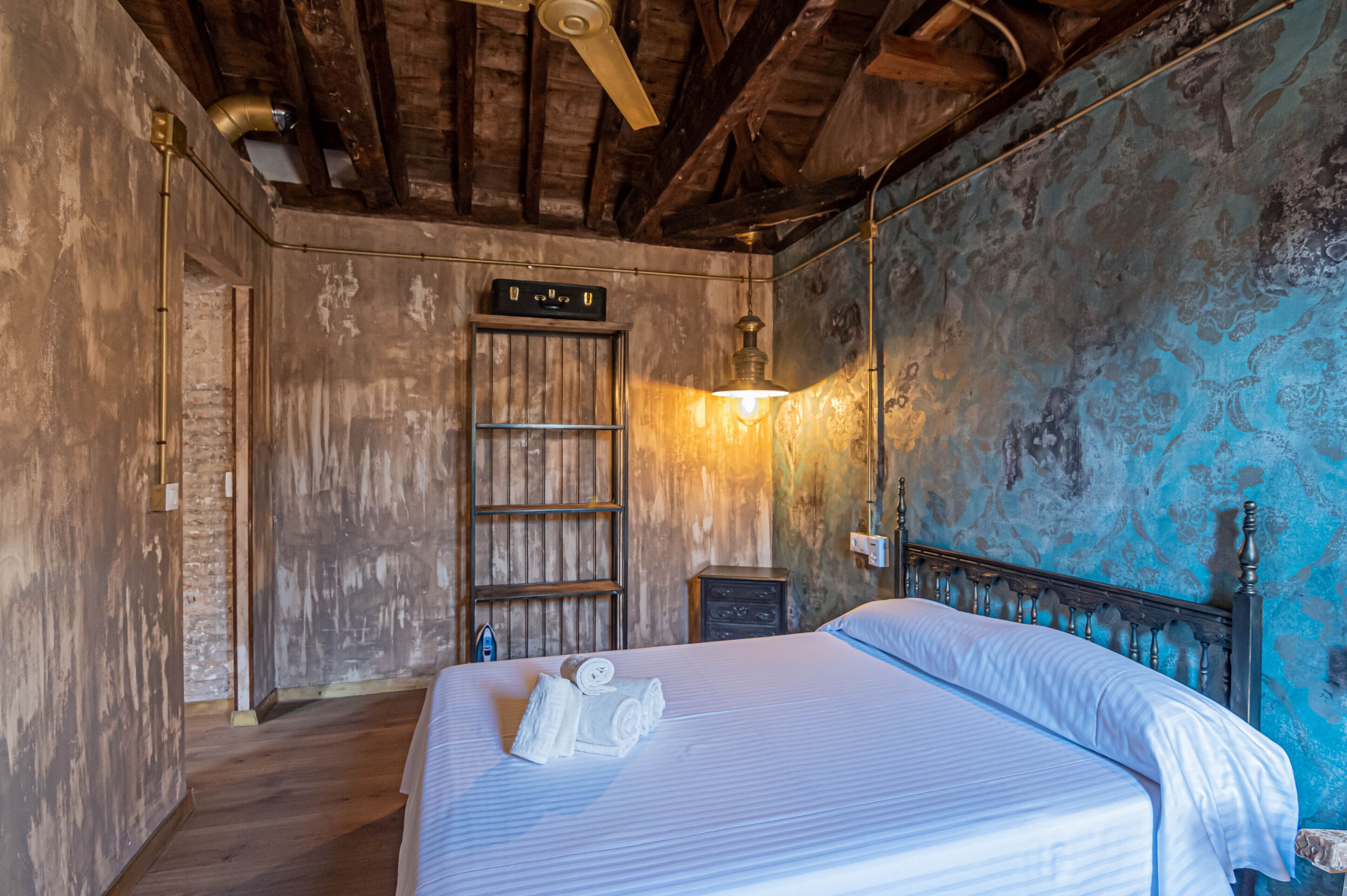 A bedroom with a wooden ceiling, a bed with white linens, a nightstand, and a wall-mounted heater.