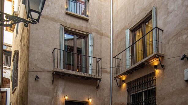 A building with a stone facade, a wooden door, and a staircase leading to the entrance. - Apartamentos CV (Granada)