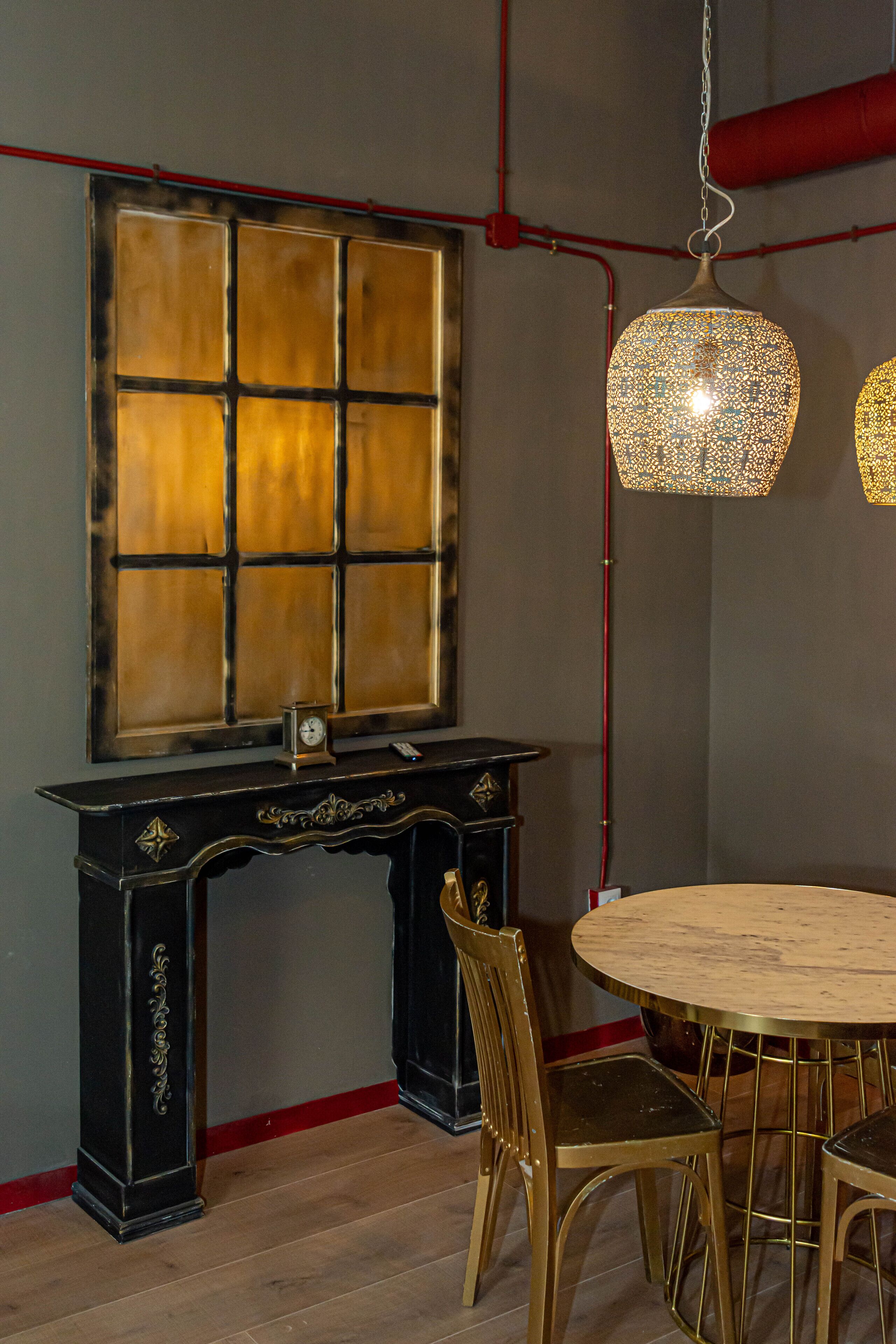A dining area with a round table, chairs, a black console table with a clock, and two hanging lamps.