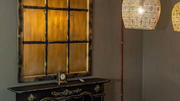 A dining area with a round table, chairs, a black console table with a clock, and two hanging lamps.