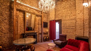 A room with a brick wall, a round glass table, a red sofa, and a chandelier. - Apartamentos CV (Granada)