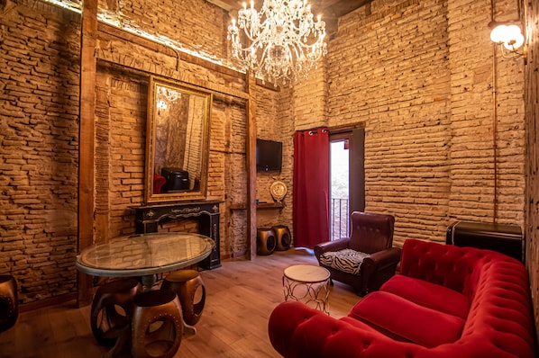 Una habitación con pared de ladrillo, una mesa redonda de cristal, un sofá rojo y una araña.