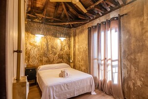 Un dormitorio con cama, vigas de madera en el techo, pared de piedra y una ventana con cortinas.
