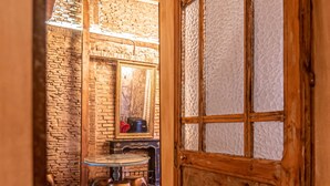 A rustic wooden room with a stone wall, a wooden door with glass panels, and a small round table with a chair. - Apartamentos CV (Granada)