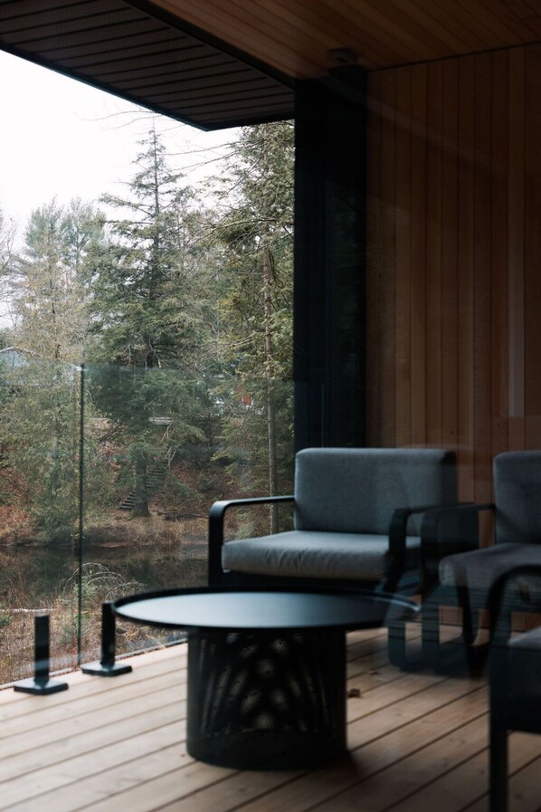 A wooden deck with a round table and two chairs, overlooking a forested area.