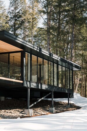 A modern cabin with large windows, a wooden deck, and a view of a forested area. - nortehaus - Nordic and Japanese inspired escape (Kawartha Lakes)