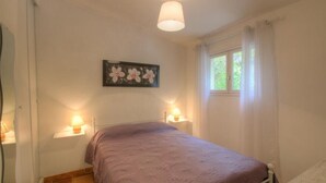 A bedroom with a bed, two bedside lamps, a window with curtains, and a wall-mounted flower painting. - Les Lauriers roses with communal swimming pool (AJACCIO)