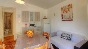 A compact living space with a kitchenette, a dining area with a fruit bowl, a sofa with a geometric pillow, and a shower area. - Les Lauriers roses with communal swimming pool (AJACCIO)
