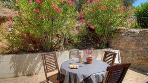 An outdoor dining area with a table and chairs, surrounded by lush greenery and flowering plants. - Les Lauriers roses with communal swimming pool (AJACCIO)