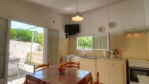 A compact kitchen with a dining table, chairs, a TV mounted on the wall, and a window with a curtain. - Les Lauriers roses with communal swimming pool (AJACCIO)