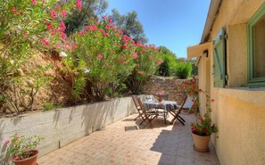 A patio with a table and chairs, surrounded by plants and a stone wall. - Les Lauriers roses with communal swimming pool (AJACCIO)