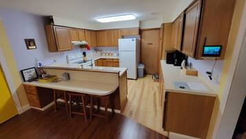 A compact kitchen with wooden cabinets, a white refrigerator, a stove, and a small bar area.