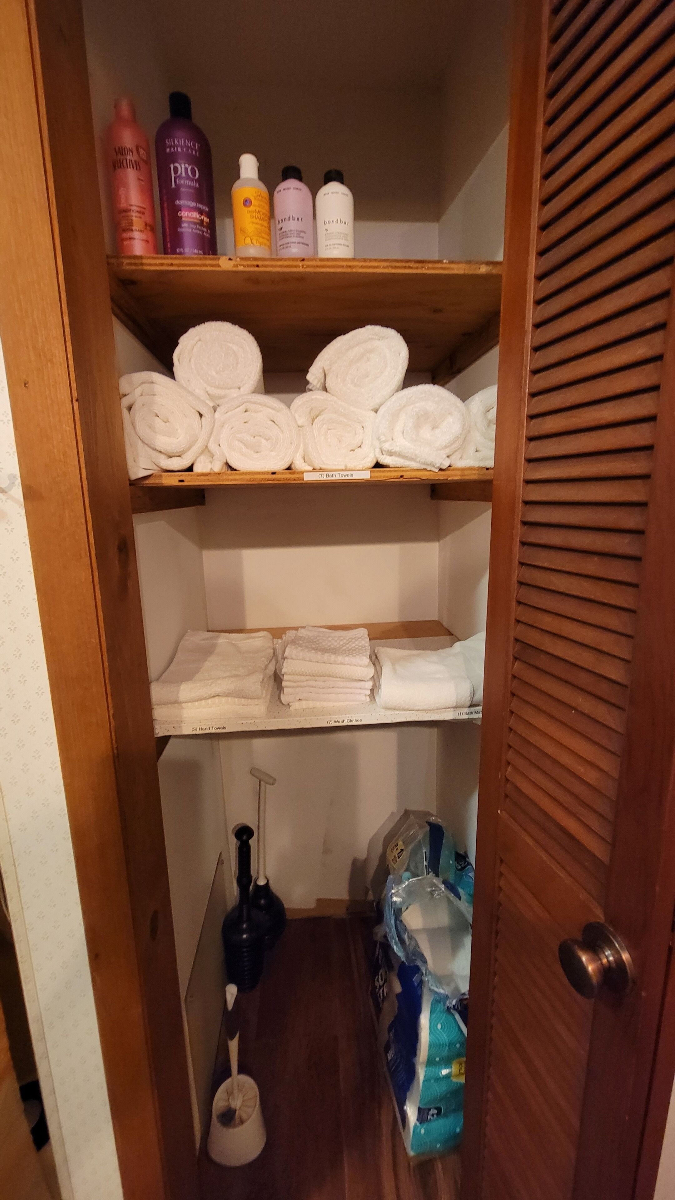 A storage closet with shelves holding various toiletries, towels, and cleaning supplies.